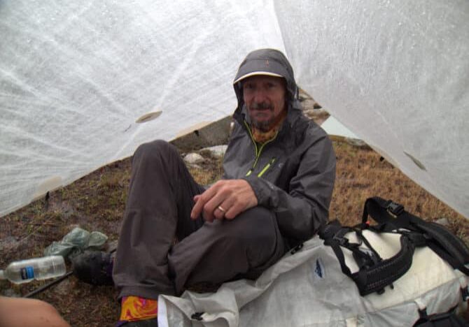 Dave hanging out under his cuben A-frame while an afternoon thunderstorm passes over the High Sierra. For irregular and short-lived rain events such as that one, his minimalist OR rain jacket was perfect.